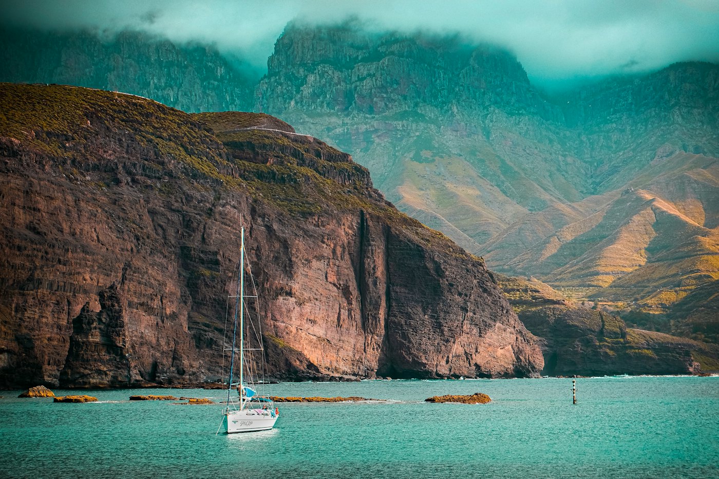 A white yacht at anchor beneath steep sea cliffs off the coast of Gran Canaria