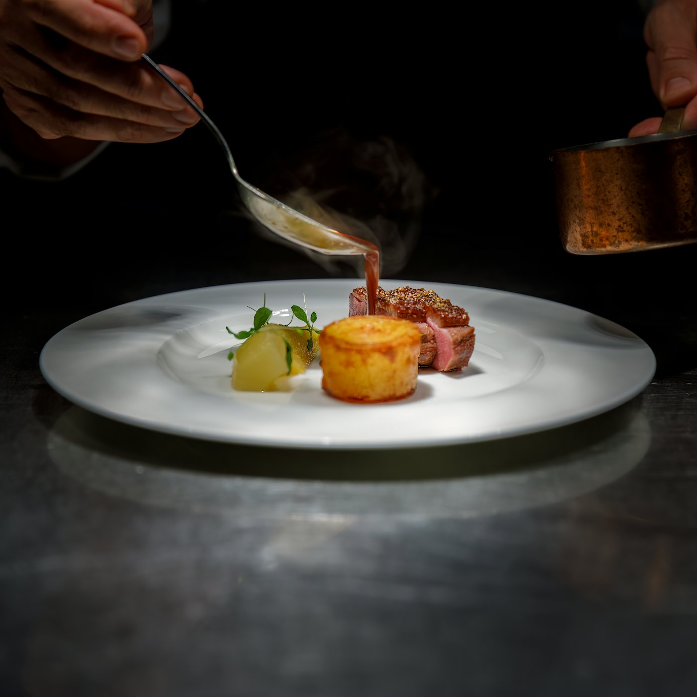 A private chef finishing a plated dish with sauce for dinner at a villa