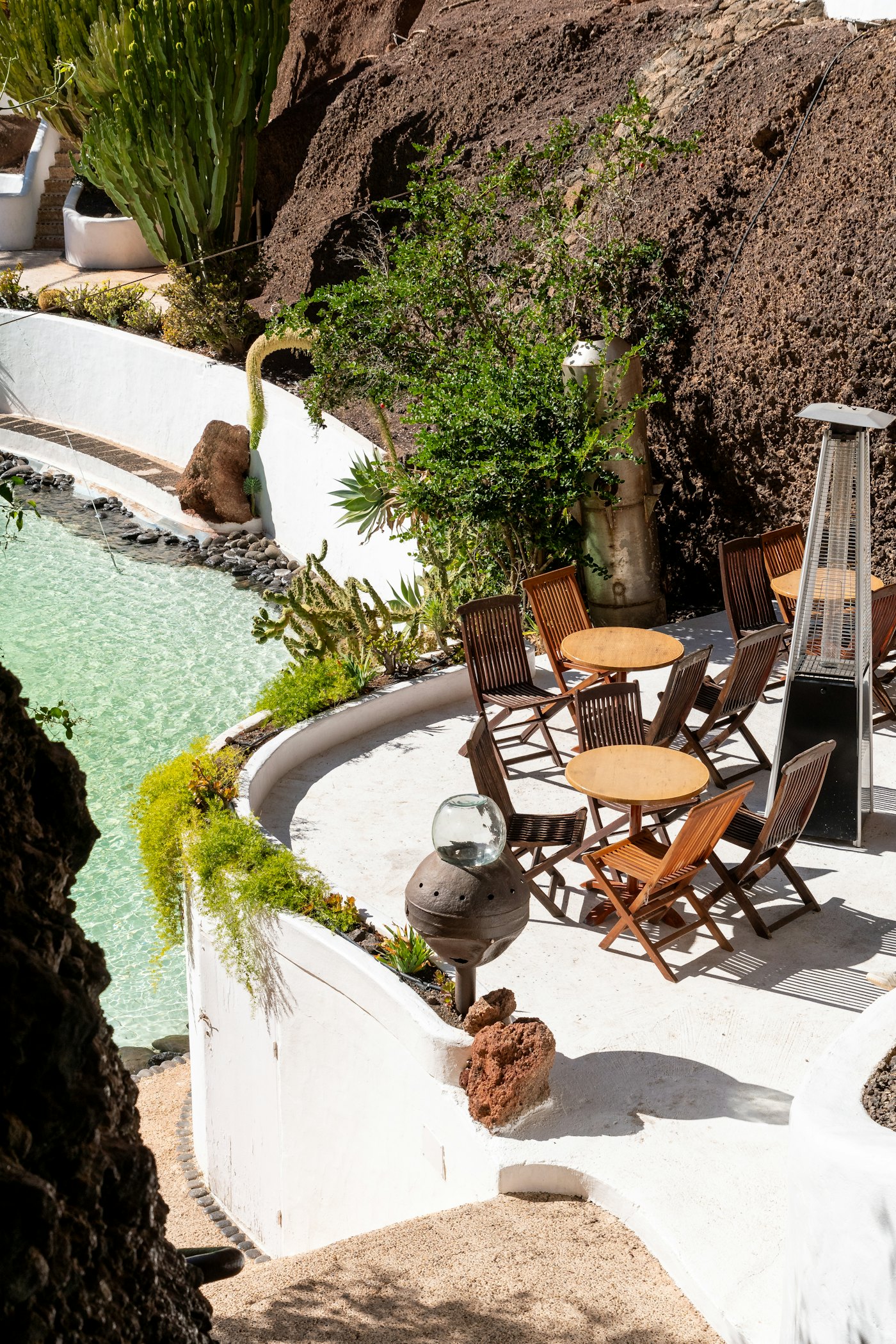 Una terraza a la sombra con la mesa puesta junto a la piscina y el jardín de una villa