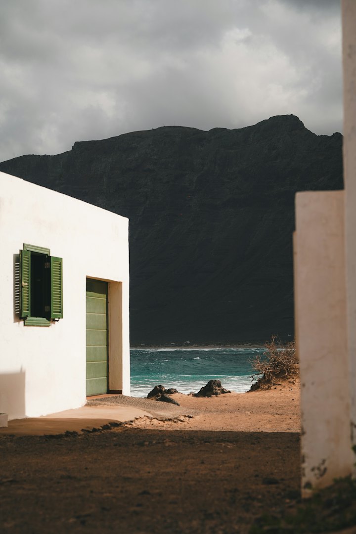 Una casa canaria encalada con contraventanas verdes sobre una costa volcánica