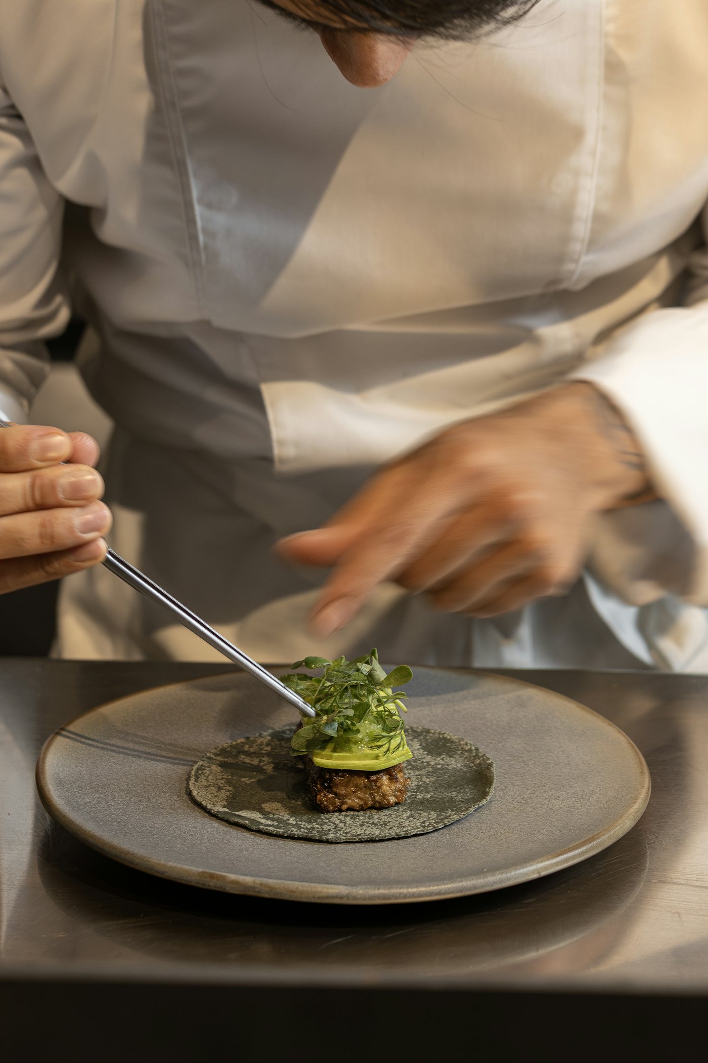 A chef plating a small dish with tweezers