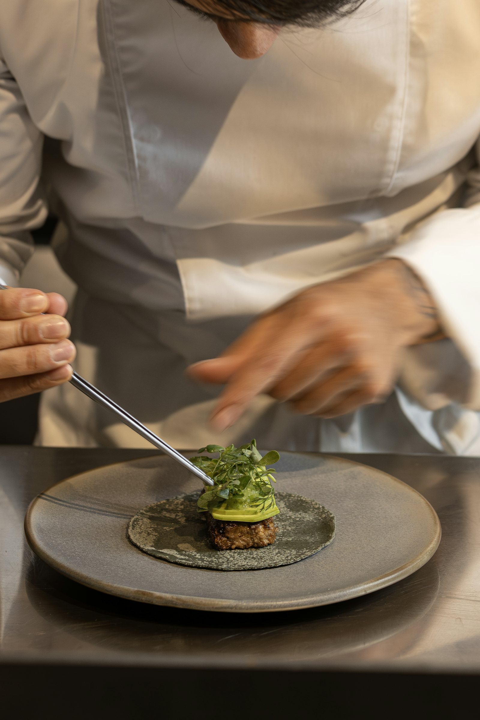 Un chef emplatando un pequeño plato con pinzas